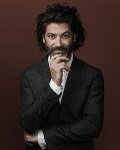 a man in a suit and tie posing for a photo with his hand on his chin