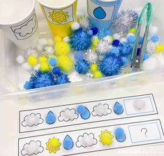 some blue and yellow pom poms are in a plastic container next to two cups