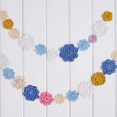 a crocheted heart is hanging on a white wall with blue, yellow and pink flowers