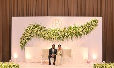 two people are sitting on a couch in front of a floral arch with candles and flowers