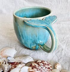 there is a blue mug with a whale tail on it next to seashells