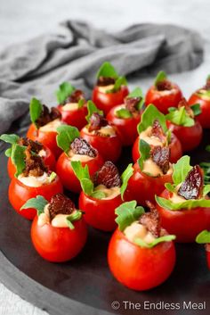 small stuffed tomatoes with bacon and green leaves on a black plate, ready to be eaten