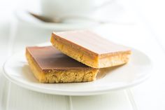 two pieces of peanut butter bars on a white plate with a cup of coffee in the background