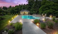 an outdoor swimming pool surrounded by landscaping and trees at dusk with lights on the walkway