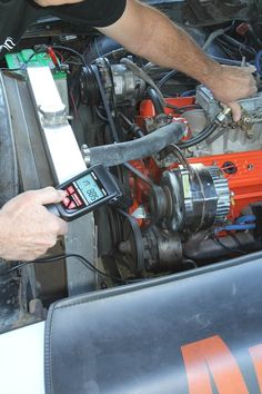 a man is working on an engine in his car with a digital thermometer