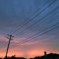 the sun is setting behind power lines and telephone poles with houses in the background at dusk