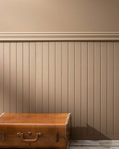 an old suitcase sitting on the floor in front of a wall with wood paneling