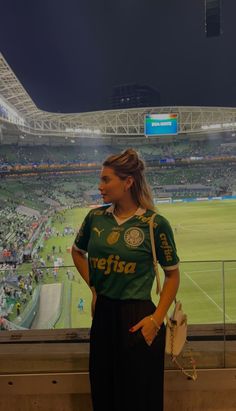 a woman standing in front of a large screen at a soccer stadium with the lights on