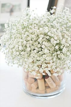 a vase filled with white flowers and corks on top of a table next to a window