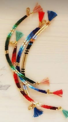 multicolored beaded bracelets with tassels and gold tone beads on white wood background