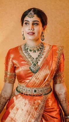 a woman in an orange and gold sari standing next to a table with flowers