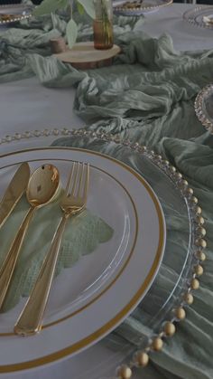 a table set with silverware and green napkins, gold rimmed cutlery