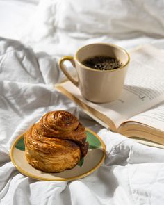 a cup of coffee sits next to a pastry on a plate and an open book