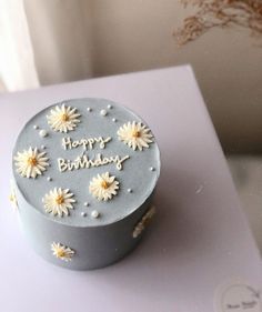 a birthday cake with daisies on it sitting on top of a white tablecloth