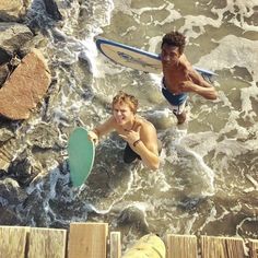 two boys are playing in the water with surfboards and one is jumping into the water