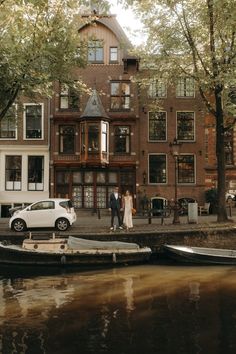 a couple standing on the dock next to some boats in front of a large building