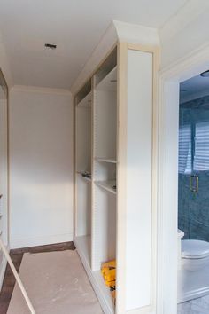 an empty bathroom with white walls and shelves on the wall, next to a toilet