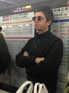 a man with his arms crossed standing in front of a poster at the subway station