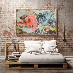 a bed with white sheets and pillows in front of a painting on a brick wall