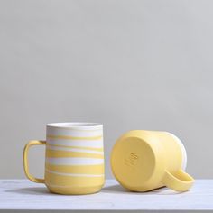 two yellow coffee mugs sitting next to each other on a white countertop against a gray wall