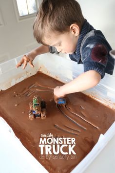 a young boy is playing with chocolate frosting in his truck themed play tray at the table