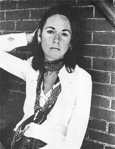 a black and white photo of a woman leaning against a brick wall with her hands on her head