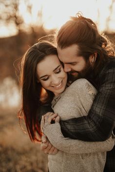 a man and woman hugging each other in an open field with the sun behind them