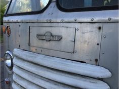 an old silver bus parked on the side of the road with its door open and it's front grill missing