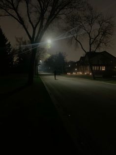 a person is walking down the street at night with lights shining on houses in the background