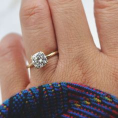 a woman's hand with a diamond ring on top of her finger and a sweater in the background