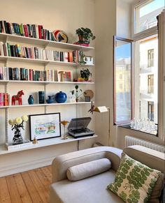 a living room filled with furniture and bookshelves next to a large window on top of a hard wood floor