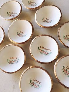 nine small white dishes with gold rims and floral designs on them, sitting on a table