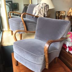 two blue chairs sitting on top of a wooden table next to a lamp and pictures