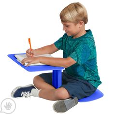 a young boy sitting at a blue table writing