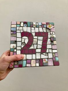 a hand holding up a piece of art made out of glass and magnets with the number seven on it