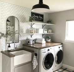 a washer and dryer in a room with white tiles on the walls, wooden counter top