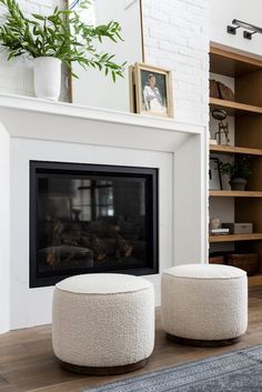 two white stools sitting in front of a fireplace