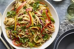 a white bowl filled with noodles and vegetables on top of a blue table cloth next to utensils