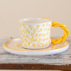 a yellow and white coffee cup sitting on top of a wooden table next to a plate