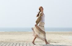 a woman walking across a wooden floor next to the ocean