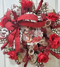 a wreath with red roses and ribbon hanging on a door frame that is decorated with an image of a woman's face