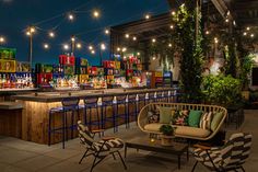 an outdoor bar with chairs, tables and lights hanging from the ceiling at night time