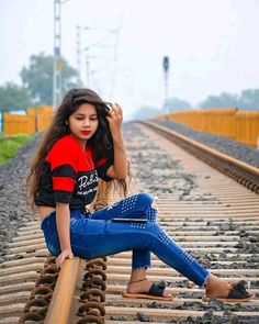 a young woman sitting on train tracks with her hand in her hair and looking at the camera