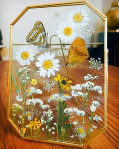 a glass box with flowers and butterflies in it on a wooden table next to a vase