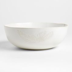 a white bowl with a design on the side and leaves in the middle, sitting on a white surface