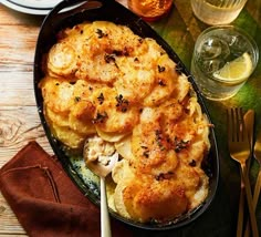 a casserole dish with potatoes and meat on a table next to silverware