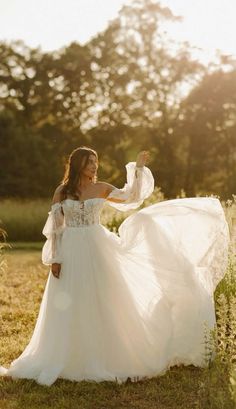 a woman in a white wedding dress is standing in the grass with her arms outstretched