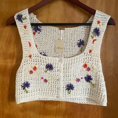 a crocheted top with flowers on it is hanging on a wooden hanger