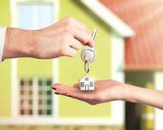 two people handing keys to each other in front of a house with a keychain