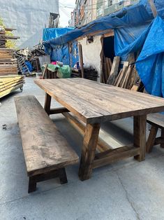 a wooden table and bench sitting in the middle of a street with blue tarps